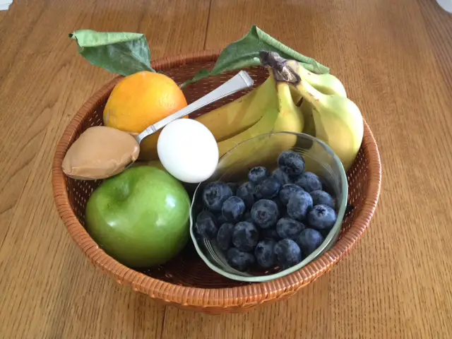 Basket filled with with fruits, a spoon of peanut butter, and a hard boiled egg