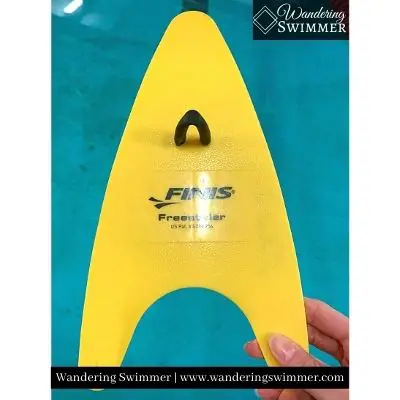 Image of a yellow, regular size FINIS Freestyler Paddle with pool water in the background