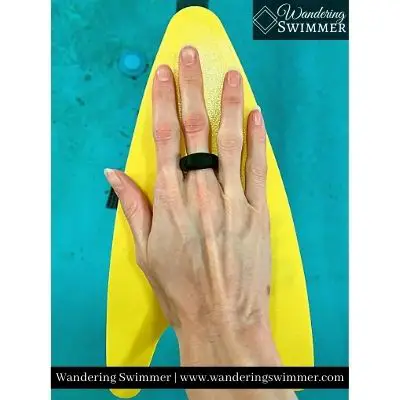 Image with a swimmer's hand wearing a single yellow, regular size FINIS Freestyler Paddle with pool water in the background