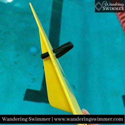 Side image of a FINIS Freestyler Paddle showing the Skeg fin on the underside of the paddle. A pool is in the background with the black line visible.