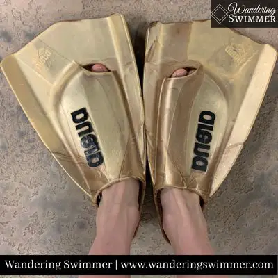 A view of a swimmer wearing golden colored Arena Pro Fins on the pool deck. Their toes are just visible from the toe hole and fit perfectly in the fins